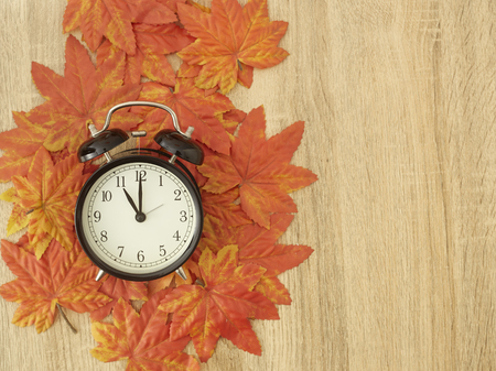 Black vintage clock with dried maple leaves on wooden . Autumn time changeの写真素材