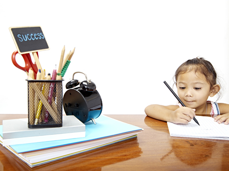 Child girl thai doing homework at home kitchen table. Space for design Sunshine comes from the left.