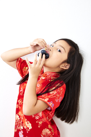 Girl child 8 years in traditional Chinese dress  New year 2019 with holding a Eating Grape bunch gestures on white wall backgroundの写真素材