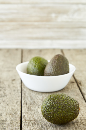 Avocado on old wooden table.Halfs on white bowl. Fruits healthy food concept. empty space. Natural morning sunshine on the left side.の写真素材