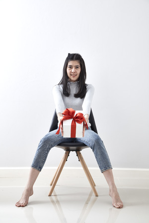 Beautiful sexy young Asian woman gift box sitting in a chair on whiteの写真素材
