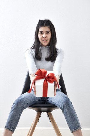 Beautiful sexy young Asian woman gift box sitting in a chair on whiteの写真素材