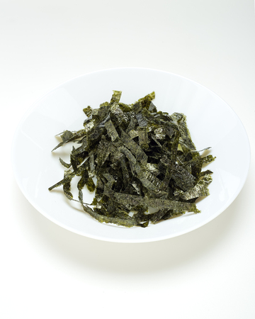 Seal of dried seaweed in a white plate on a white table. Light emulates natural light with space for design.の写真素材