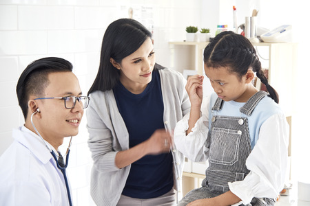 The doctor listens to the lungs of a sick boy in a stethoscope. He came with his mother to the doctor. The girl is ill with a cold. They are in the light office of the doctor.の写真素材