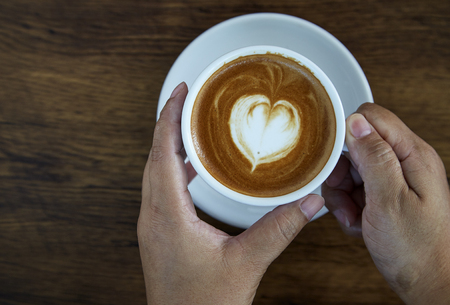 Hands holding coffee cup heart on coffee cup and woman nails on wood, valentine love concept.の写真素材