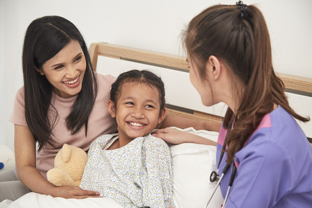 Female doctor and Young asian little patient with and mother smiling while doctor come to visitの写真素材