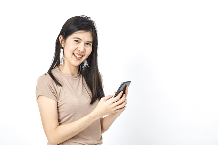 Asian Portrait of a smiling young woman holding mobile phone and looking up at copyspace isolated wall over greyの写真素材