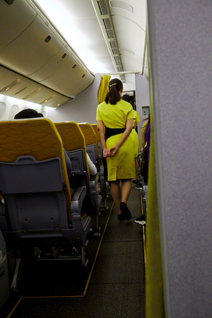 Interior of commercial airplane with Flight attendant serving passengers  on seats during flight. Stewardess in dark Yellow uniform walking the aisleの写真素材