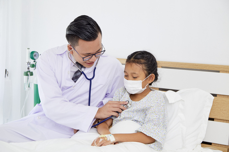 The young doctor takes care of talking to the patient, the girl on the hospital bed. Medical care conceptの写真素材