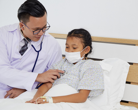 The young doctor takes care of talking to the patient, the girl on the hospital bed. Medical care conceptの写真素材