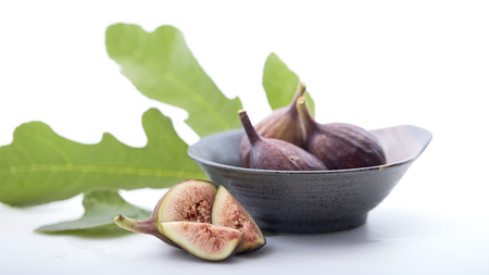 Fresh figs in a a bowl with fig leaf on white table. Healthy snack and food. empty space for text