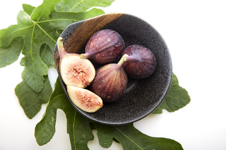 Fresh figs in a a bowl with fig leaf on white table. Healthy snack and food. empty space for text
