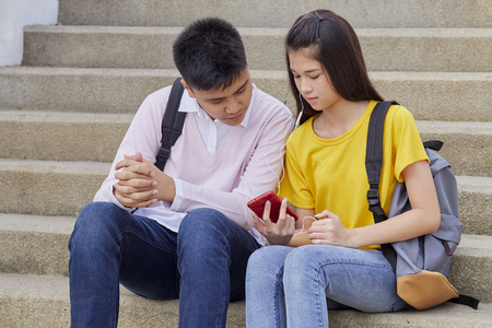 Girl and boy teens playing on mobile phones and listening to music in the city, hipster style, students, friends together, smiling happy, holding smartphone, listening to music on earphonesの写真素材