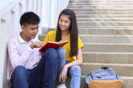Attractive Asian Student sitting stairs at outdoor place. Couple people using book and laptop with Attractive Smiling. People with Education Concept.の写真素材