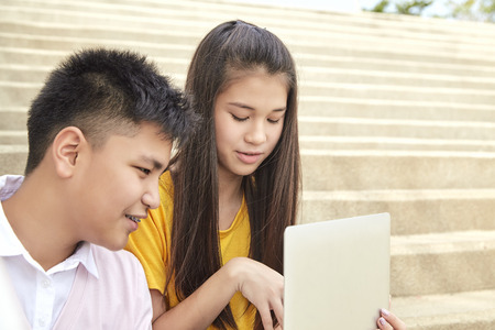 Teenager boy and girl sitting on stair and using notebook computer at school in a park, Young generation and Education conceptの写真素材