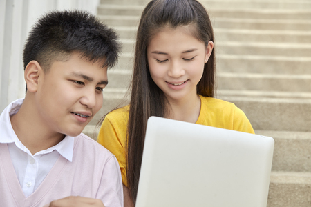 Teenager boy and girl sitting on stair and using notebook computer at school in a park, Young generation and Education conceptの写真素材