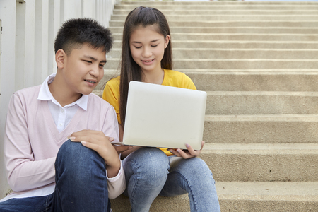 Teenager boy and girl sitting on stair and using notebook computer at school in a park, Young...