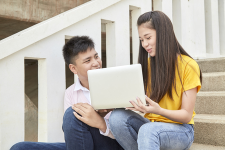 Teenager boy and girl sitting on stair and using notebook computer at school in a park, Young generation and Education conceptの写真素材