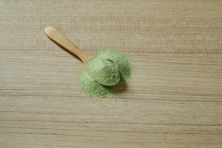 Wooden spoon with powdered matcha green tea on table