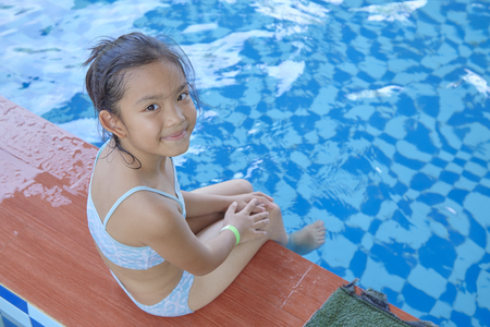 Happy little asian girl sitting at the edge of a swimming pool, summer vacation conceptの写真素材