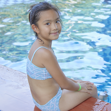 Happy little asian girl sitting at the edge of a swimming pool, summer vacation conceptの写真素材