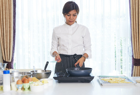 Smiling young asian woman cook sweet cake in the kitchenの写真素材