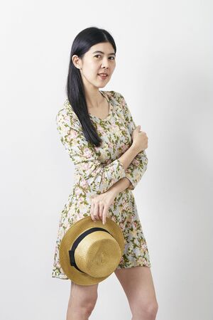 Attractive nice cute portrait  Asian young woman in floral spring summer dress with hat. Girl posing on a white background. Travel fashion conceptの写真素材