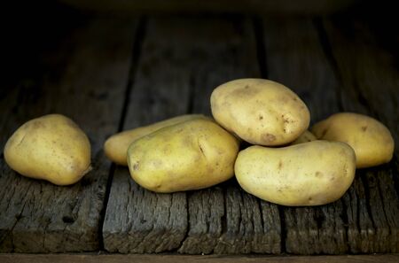 Fresh potatoes heap on an old wooden table, on rustic wooden background. Fresh organic food. Organic food, carbs, tubers.の写真素材