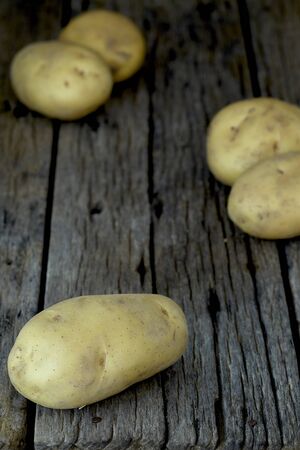 Fresh potatoes heap on an old wooden table, on rustic wooden background. Fresh organic food. Organic food, carbs, tubers.の写真素材