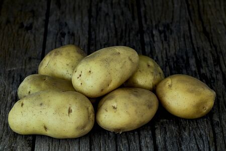 Fresh potatoes heap on an old wooden table, on rustic wooden background. Fresh organic food. Organic food, carbs, tubers.の写真素材
