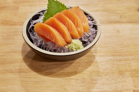 Close-up shot sashimi salmon in black bowl with ice, vegetables and wasabi on wooden backgroundの写真素材