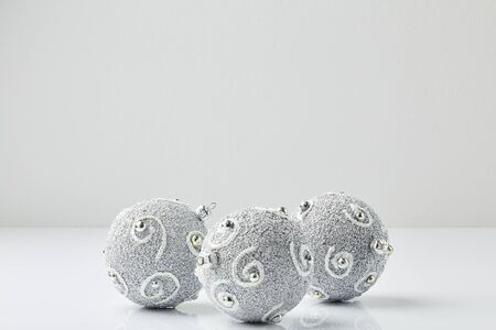 Three Silver Christmas Balls With Glitter Stripes On the white table, the room wall is light grayの写真素材