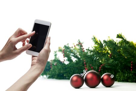 Mockup image of a female hand holding white mobile phone with blank black screen with christmas decorations big sale background. copy space for textの写真素材