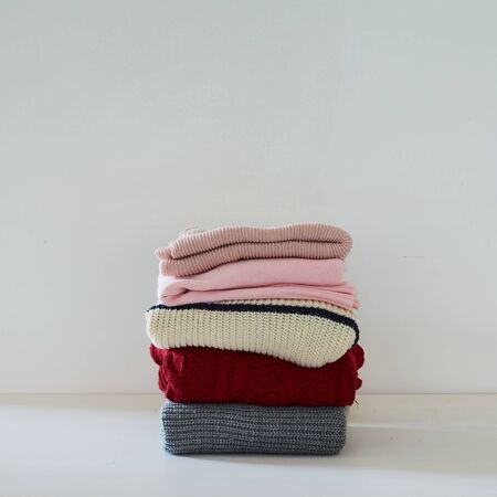 Pile of knitted winter clothes on white table, sweaters, copy space for textの写真素材