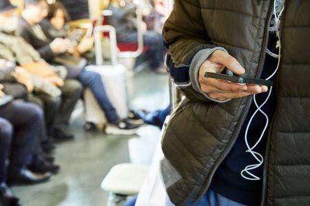 Mockup image of hand holding white mobile phone with blank black screen in subway with many people...