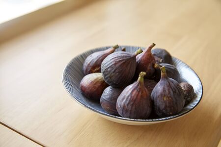 Ripe juicy purple figs berries in dish isolated on wooden table background