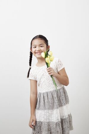 Asian little girl holding a bouquet of yellow tulips on white background. Concept of holidaysの写真素材