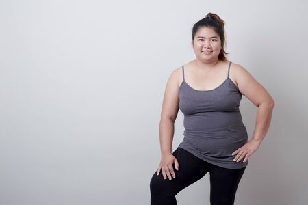 Beautiful fashionable plump asian woman in exercise clothes standing on isolated bright grey background, Healthy exercise conceptの写真素材