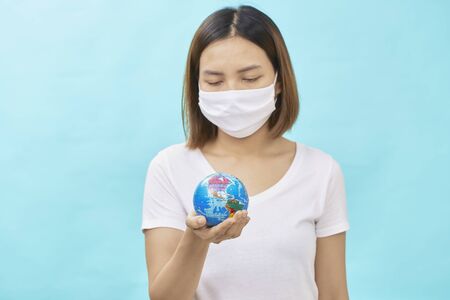 Young asian women wearing protective masks holding a safe world on blue background.safe at home. Protection against coronavirus Covid-19.の写真素材