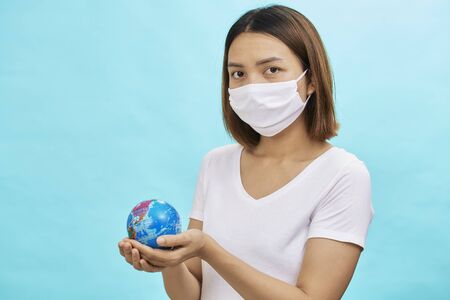 Young asian women wearing protective masks holding a safe world on blue background.safe at home. Protection against coronavirus Covid-19.の写真素材