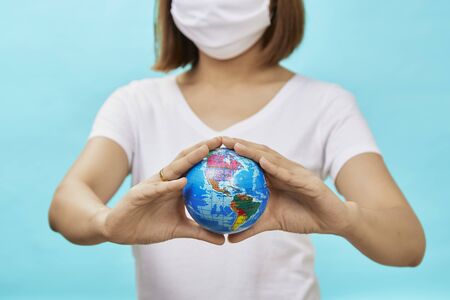 Young asian women wearing protective masks holding a safe world on blue background.safe at home. Protection against coronavirus Covid-19.の写真素材