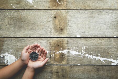 Child hands holiding compass on dark wooden background top view copy space, Choose direction concept.の写真素材