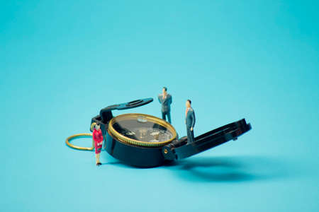 Miniature businessman and compass on bright blue backgroun