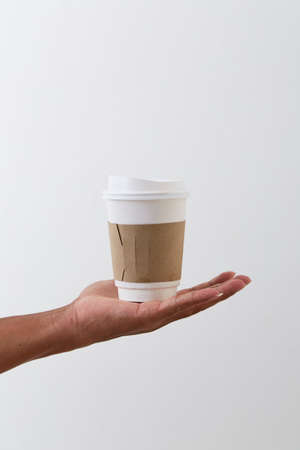 Mockup of male hand holding a coffee paper cup isolated on light grey background.