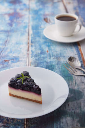 Piece of blueberry cheese cake on white plate on wood background
