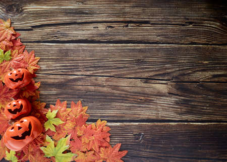 Halloween pumpkins with autumn fall leaves over wooden background