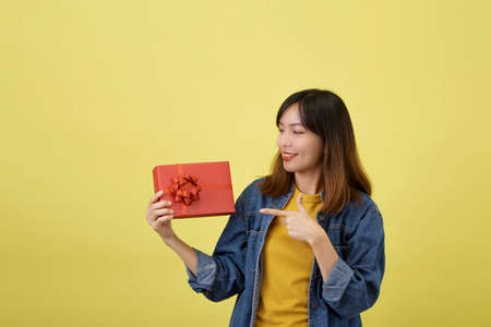 Portrait beautiful young asian woman with red gift box on yellow isolated backgroundの写真素材