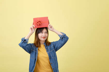 Portrait beautiful young asian woman with red gift box on yellow isolated background