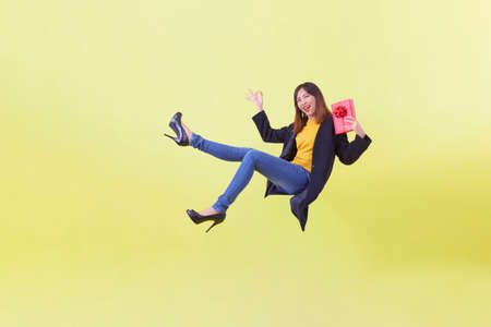 Full length portrait Attractive young woman holding gift levitating isolated yellow backgroundの写真素材