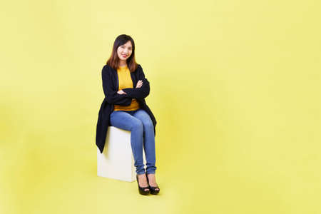 attractive young Asian woman sitting on the blank empty box on yellow background For job hunting ideasの写真素材